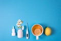 Medical electronic thermometer, medication bottle with pills, spray for nose and tea with lemon on blue background.