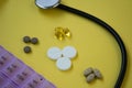 Bunch of pills and capsules, box for storage of drugs and medical stethoscope and blood pressure meter on yellow background, healt