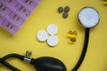 Bunch of pills and capsules, box for storage of drugs and medical stethoscope and blood pressure meter on yellow background, healt