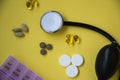Bunch of pills and capsules, box for storage of drugs and medical stethoscope and blood pressure meter on yellow background, healt
