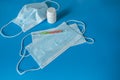 Medical face mask covering mouth and nose, pills, thermometer for measuring body temperature on a blue background.