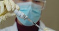 Medical with face mask filling a syringe with vaccine. Close up of a researcher with face mask filling up a syringe with