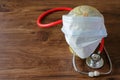 Medical face mask with world globe on and medical stethoscope on wooden table.