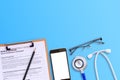 Medical form with smart phone and blue stethoscop on wooden desk