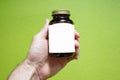 A medical glass bottle of brown color with a white label for your text and a bronze metal cap in a male hand