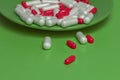 medical green background.Capsules of red and white flowers pour out from a green plate on a green background.