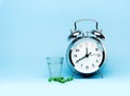 Medical green capsule pills, glass water and alarm clock on blue background. Royalty Free Stock Photo