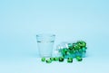 Medical green pill capsules in a glass bottle and a glass of water on a blue background. Royalty Free Stock Photo