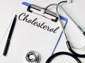 Phrase CHOLESTEROL written on paper clipboard with stethoscope and a pen.