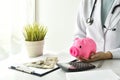 Medical and health insurance concept, Doctor holding piggy bank and money in hospital background.