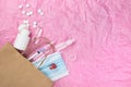 Medical items such as ampoule pills, a syringe and a mask peek out of a paper bag against a background of pink crumpled paper. Royalty Free Stock Photo