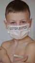 Medical mask on the child`s face. On the white mask is a black inscription Coronavirus. The blond boy is careful of the