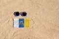 A medical mask in the color of the Canary Islands flag lies on the sandy beach next to the glasses.