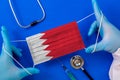 Medical mask with the flag of Bahrain in the hands of a doctor and stethoscope, flat lay.