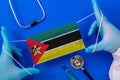 Medical mask with the flag of Mozambique in the hands of a doctor and stethoscope, flat lay.