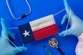 Medical mask with the flag of Texas in the hands of a doctor and stethoscope, flat lay.
