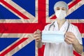 Medical mask in the hands of a doctor against the background of the national flag of Great Britain, concept of protection against