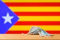A medical mask lies on the table against the background of the flag of Catalonia.
