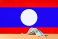 A medical mask lies on the table against the background of the flag of Laos.