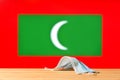 A medical mask lies on the table against the background of the flag of Maldives.