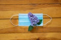 Medical mask lies on a wooden table and next to a lilac branch clos- up, flower on a medicial mask