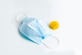 A medical mask and a spring dandelion on a white table