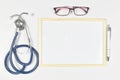 Medical mock-up with blank sheet of paper, clipboard, stethoscope, glasses on doctor desk. Health care concept. Top view