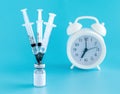 Medical needles stuck in the bottle with the vaccine, alarm clock. Vaccination against the flu, infections, covid-19 Royalty Free Stock Photo