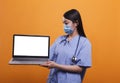 Medical nurse wearing facemask and stethoscope while holding whitescreen isolated display chroma key laptop.