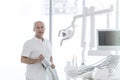 Portrait of senior dentist standing by chair at dental clinic