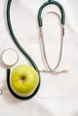 Medical phonendoscope on a medical dressing gown. A green apple is a daisy flower. Concept of health