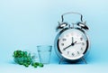 Medical pills, glass water and metal alarm clock on a blue background Royalty Free Stock Photo