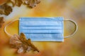 A medical protective mask and yellow dry oak leaves lie on a bright autumn background.