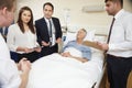 Medical Staff On Rounds Standing By Male Patient's Bed