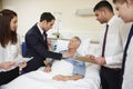 Medical Staff On Rounds Standing By Male Patient's Bed