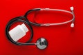 Medical stethoscope of black color and pills in jar on clean red background. Layout for the designer