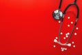 Medical stethoscope of black color and pills in jar on clean red background. Layout for the designer
