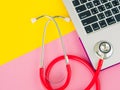 A medical stethoscope and a laptop on a pink and yellow table background.