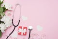 Medical stethoscope with red gift box, flowers roses and white hearts on pink background