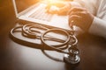 Medical Stethoscope Resting on Desk As Male Hands Type on Computer Keyboard. Royalty Free Stock Photo