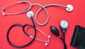 Medical stethoscopes and sphygmomanometer on red background, top view Royalty Free Stock Photo