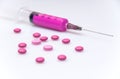 A medical syringe with a purple solution lies on a whitish background surrounded by pills Royalty Free Stock Photo