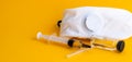 Medical syringe and white respirator on a yellow background