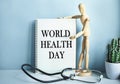 Medical table with a wooden person along with a stethoscope. Inscription WORLD HEALTH DAY on the clipboard with the holder. Health