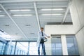 Male scientist in lab coat holding rolled plan and adjusting sleeve on glass mezzanine in atrium Royalty Free Stock Photo