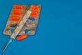 Medical thermometer and color pills on a blue background