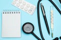 Medical thermometer and phonendoscope with pills in used blister on a blue desk in the therapist`s office with pen. Medical Royalty Free Stock Photo