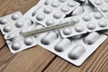 Medical thermometer and tablets in silvery blisters on a wooden table