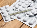 Medical thermometer and tablets in silvery blisters on a wooden table.