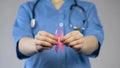 Medical worker in blue uniform holding pink ribbon in hands, breast cancer risk